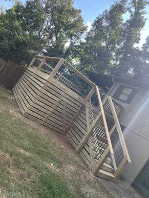 Interior view of a screened-in wooden porch with a vaulted ceiling, ceiling fan, and black metal balusters overlooking a backyard.