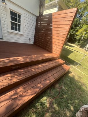 A freshly stained dark wood deck with a rich reddish-brown finish next to a house with grey siding.