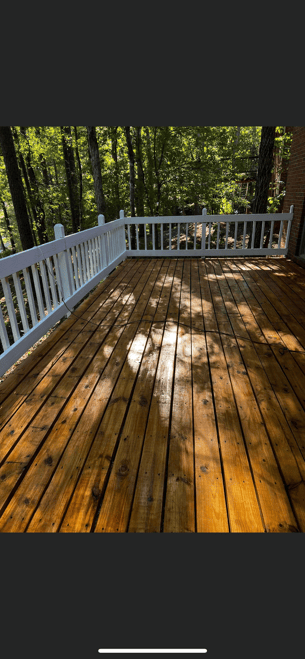 A freshly stained dark wood deck with a rich reddish-brown finish next to a house with grey siding.