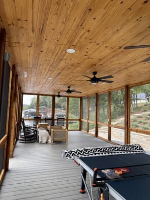 A covered porch with freshly stained dark wood floors, white railings, a hanging swing, and a wicker chair.