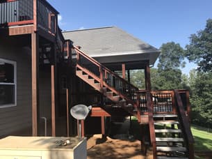 Interior view of a screened-in wooden porch with a vaulted ceiling, ceiling fan, and black metal balusters overlooking a backyard.