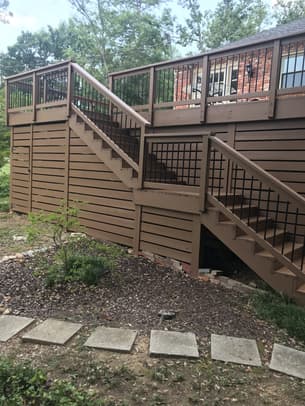 Interior view of a screened-in wooden porch with a vaulted ceiling, ceiling fan, and black metal balusters overlooking a backyard.