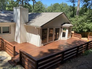 A screened-in porch with dark stained wood ceilings, skylights, and wicker furniture overlooking a wooded backyard.