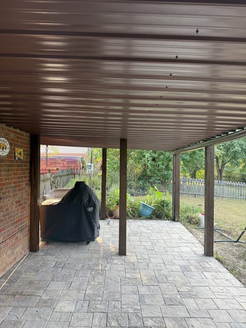 Interior view of a screened-in wooden porch with a vaulted ceiling, ceiling fan, and black metal balusters overlooking a backyard.