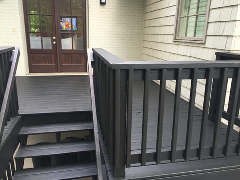 A freshly stained dark wood deck with a rich reddish-brown finish next to a house with grey siding.
