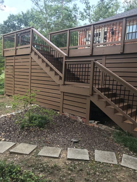 Newly stained wooden deck stairs with black metal railings and a warm honey finish.