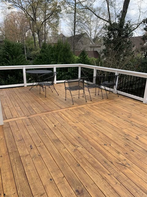 Newly stained wooden deck stairs with black metal railings and a warm honey finish.